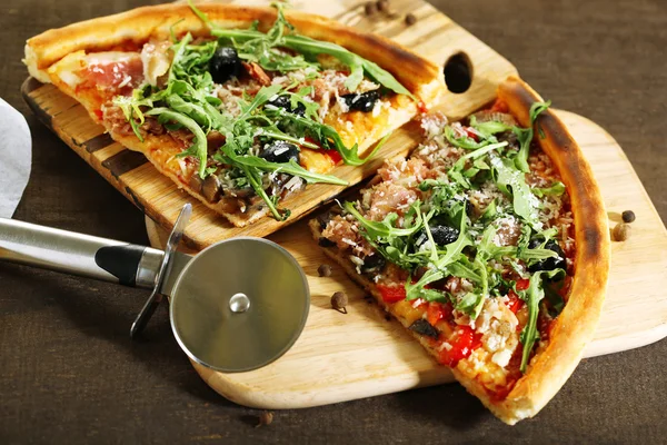 Trozo de pizza con rúcula en la tabla de cortar, sobre fondo de madera de color —  Fotos de Stock