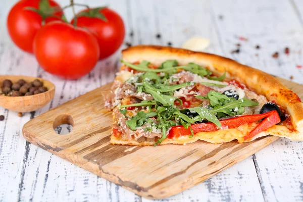 Piece of pizza with arugula on cutting board, color wooden background — Stock Photo, Image