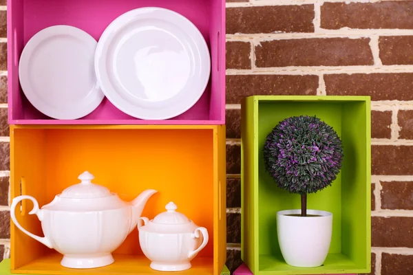 Prateleiras coloridas bonitas com utensílios de mesa no fundo da parede marrom — Fotografia de Stock