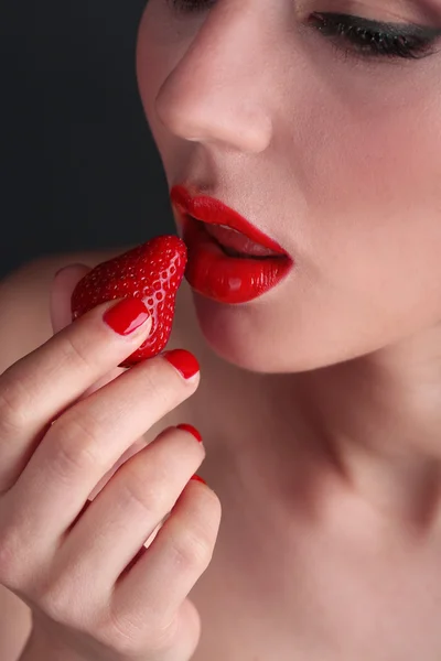 Meisje met rode lippen, nagels en aardbeien op donkere achtergrond — Stockfoto