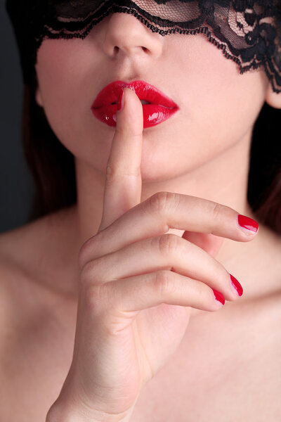 Girl with red lips, nails and openwork black eye on dark background