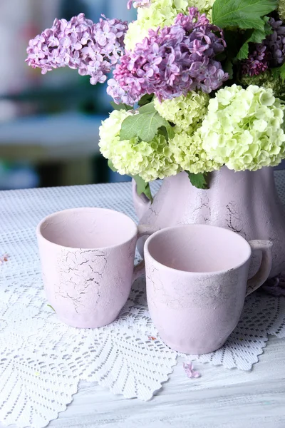 Composición con tazas de té y hermosas flores de primavera en jarrón, sobre mesa de madera, sobre fondo brillante — Foto de Stock