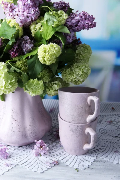 Composición con tazas de té y hermosas flores de primavera en jarrón, sobre mesa de madera, sobre fondo brillante —  Fotos de Stock