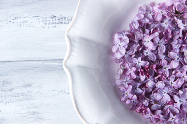 Beautiful lilac flowers on white plate on color wooden background