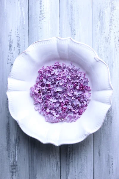 Hermosas flores lila en plato blanco sobre fondo de madera de color —  Fotos de Stock