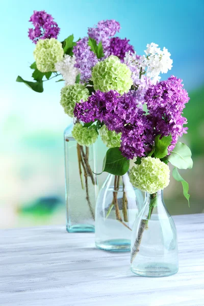 Lindas flores de primavera em garrafas de vidro, na mesa de madeira, no fundo brilhante — Fotografia de Stock