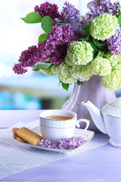 Composición con tetera, taza y hermosas flores de primavera en jarrón, sobre mesa de madera, sobre fondo brillante — Foto de Stock