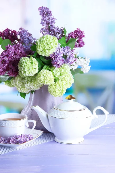 Composición con tetera, taza y hermosas flores de primavera en jarrón, sobre mesa de madera, sobre fondo brillante — Foto de Stock