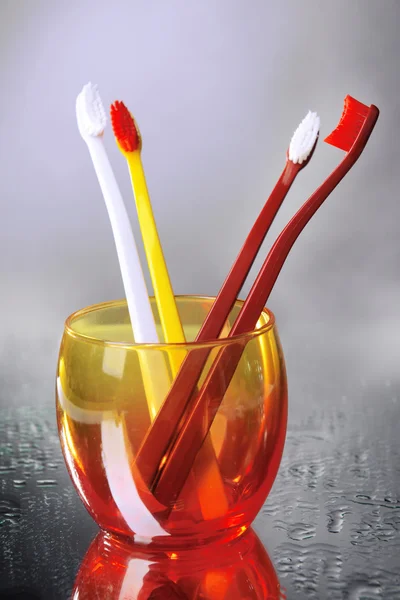 Az üveg, a szürke háttér fogkefék — Stock Fotó