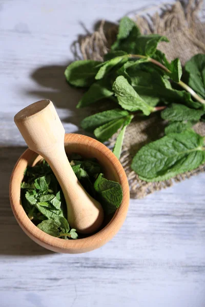 Sammansättning med trä murbruk och mynta blad på färg trä bakgrund — Stockfoto