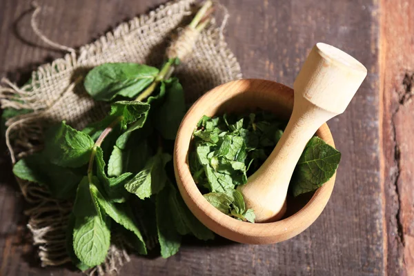 Sammansättning med trä murbruk och mynta blad på färg trä bakgrund — Stockfoto