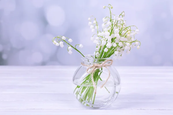 Beaux lys de la vallée dans un vase en verre sur une table en bois — Photo