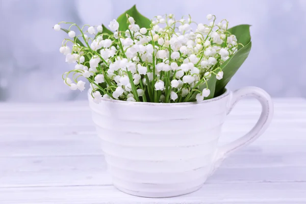 Beautiful lilies of the valley in cup on wooden table — Stock Photo, Image