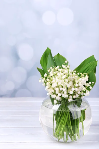 Beaux lys de la vallée dans un vase en verre sur une table en bois — Photo