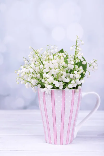 Beautiful lilies of the valley in cup on wooden table — Stock Photo, Image