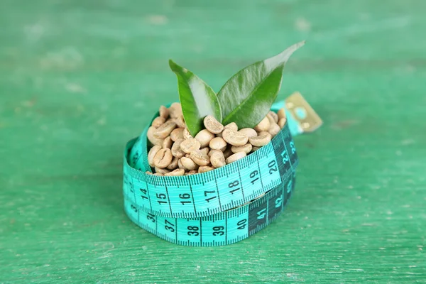 Raw green coffee beans and measuring tape, on color wooden background. Concept of weight loss — Stock Photo, Image