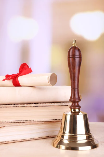 Gold retro school bell with books on table on bright background — Stock Photo, Image