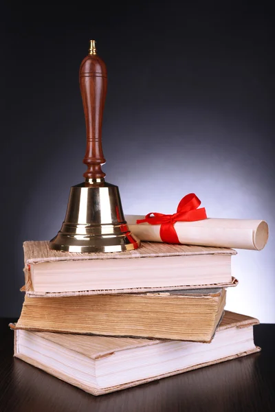 Gold retro school bell with books on table on dark background