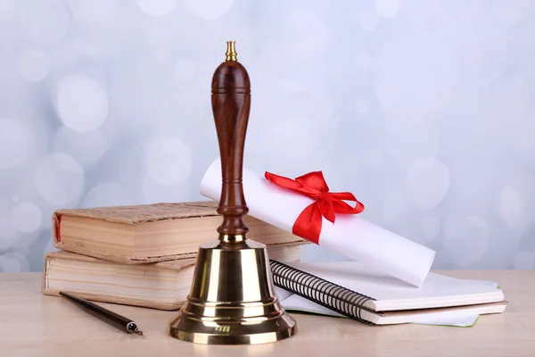 Gold retro school bell with books on table on bright background — Stock Photo, Image