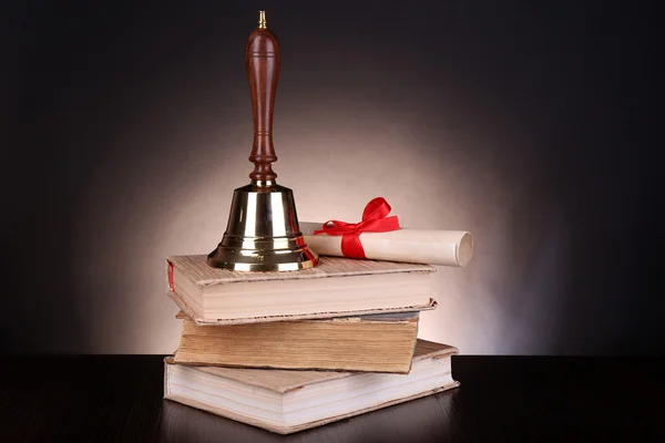Gold retro school bell with books on table on dark background — Stock Photo, Image