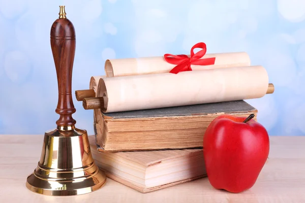 Gold school bell with school supplies on table on bright background