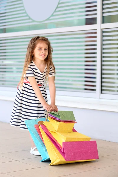 Bonne petite fille avec des sacs de magasin, en plein air — Photo