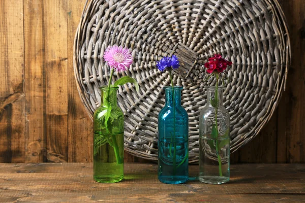Bright wildflowers in bottles on wooden background — Stock Photo, Image