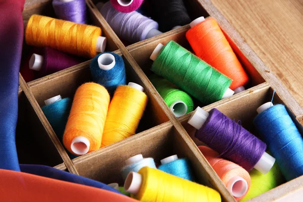 Multicolor sewing thread in wooden box, on wooden background, close-up — Stock Photo, Image