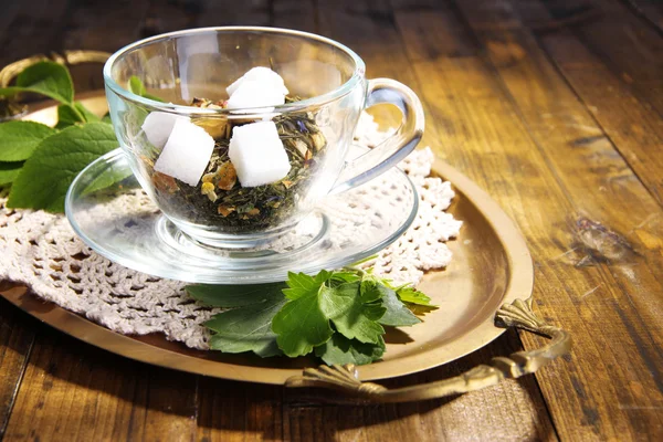 Coppa di vetro con fiori secchi ed erbe aromatiche, ingredienti di frutta per il tè, su vassoio, su sfondo di legno a colori — Foto Stock