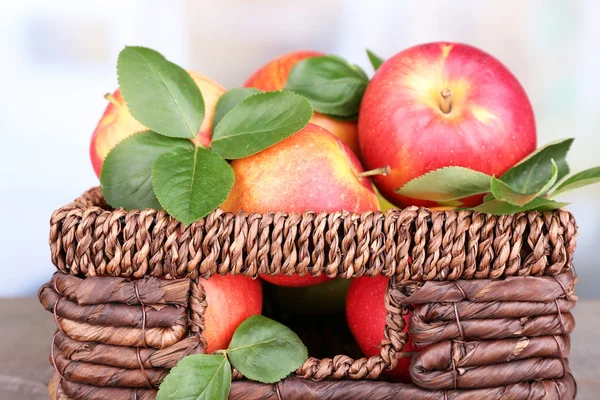 Zralé sladké jablka s listy v proutěné bedny na světlé pozadí — Stock fotografie
