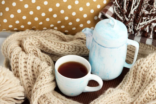 Чашка и чайник с шарфом на кровати вблизи — стоковое фото