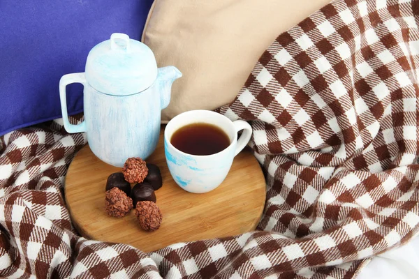 Cup en theepot met snoepjes op houten voet op bed close-up — Stockfoto