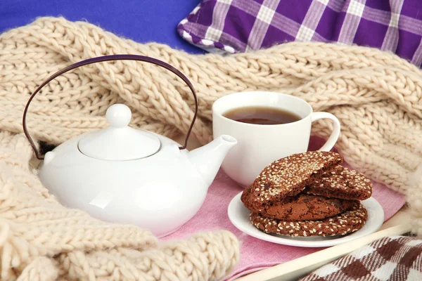 Cup and teapot with cookies on tray and scarf on bed close up — Stock Photo, Image