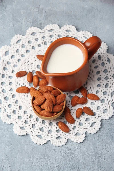 Latte di mandorla in brocca con mandorle in ciotola, su sfondo di legno a colori — Foto Stock