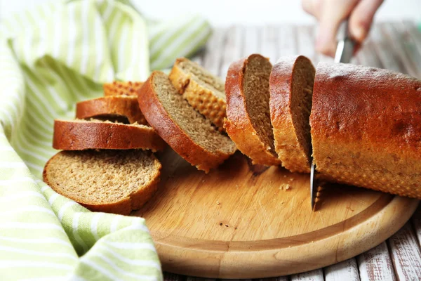 Vrouwelijke handen die brood snijden op houten plank, close-up — Stockfoto