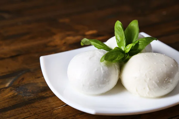 Smakelijke mozzarella kaas met basilicum op plaat op houten achtergrond — Stockfoto