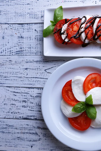 Ensalada Caprese con queso mozarella, tomates y albahaca en platos, sobre fondo de mesa de madera — Foto de Stock