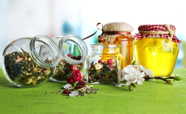 Assortment of herbs and tea in glass jars on wooden table, on bright background — Stock Photo, Image