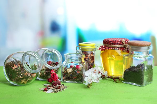 Assortiment d'herbes et de thé dans des bocaux en verre sur table en bois, sur fond lumineux — Photo