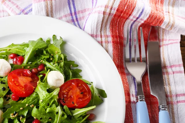 Зеленый салат из рукколы, помидоров, сыра моцарелла шарики и кунжута на тарелке, на деревянном фоне — стоковое фото