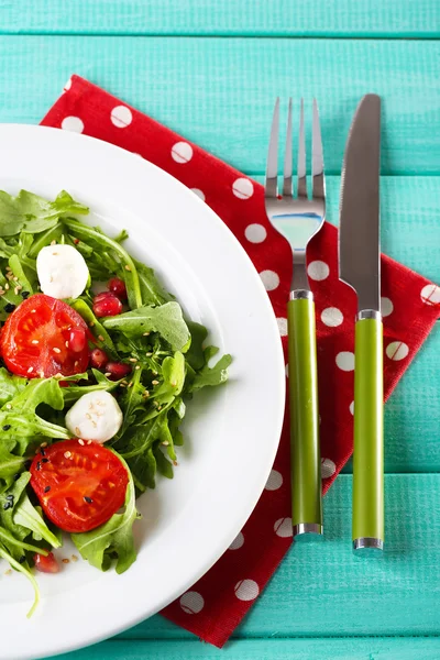 Salada verde feita com arugula, tomates, bolas de mussarela de queijo e gergelim na placa, na cor de fundo de madeira — Fotografia de Stock