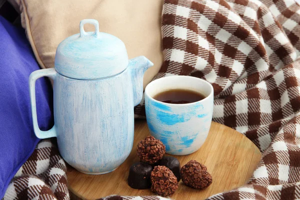 Cup en theepot met snoepjes op houten voet op bed close-up — Stockfoto