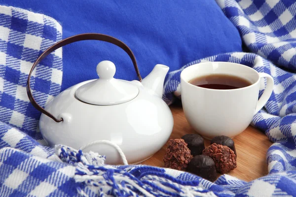 Cup and teapot with candies on wooden stand on bed close up — Stock Photo, Image