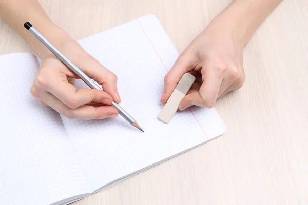 Insan eli kalem kağıt ve erase kauçuk ahşap masa arka plan üzerinde yazma ile — Stok fotoğraf