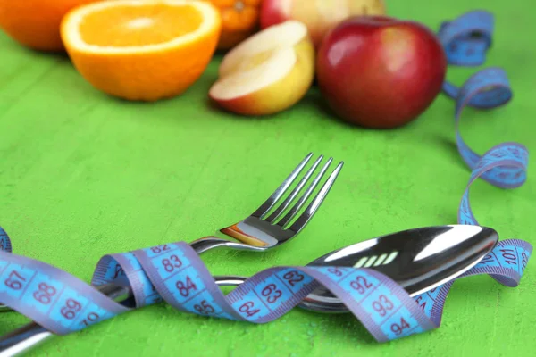 Cutlery tied with measuring tape and fruits on wooden background — Stock Photo, Image