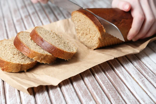 Mãos femininas cortando pão na placa de madeira, close-up — Fotografia de Stock