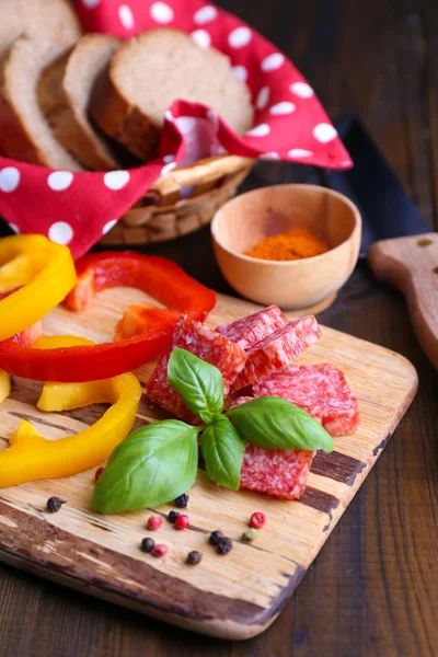 Sammansättning med kniv, välsmakande salami korv, skivat bröd och peppar på skärbräda, på trä bakgrund — Stockfoto