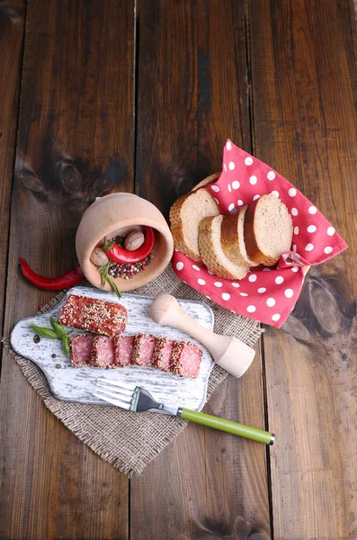 Composición de cuchillo, salchicha de salami en rodajas con sésamo, sobre tabla de cortar, sobre fondo de madera — Foto de Stock