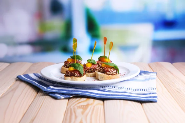 Smakelijke canapeetjes met salami, peper en basilicum bladeren, op plaat, op houten tafel, op lichte achtergrond — Stock Fotó