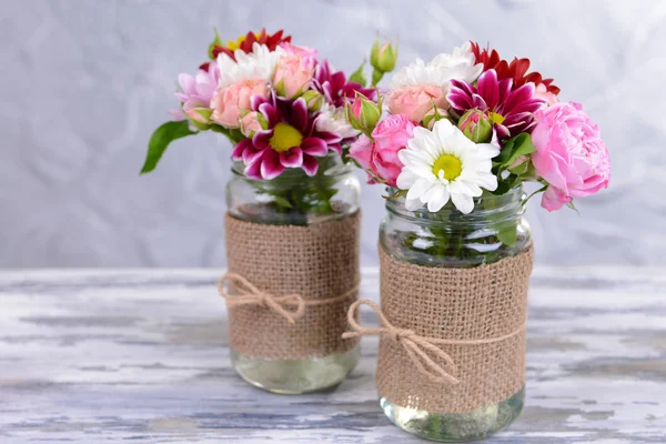 Vacker bukett av ljusa blommor i burkar på bordet på grå bakgrund — Stockfoto